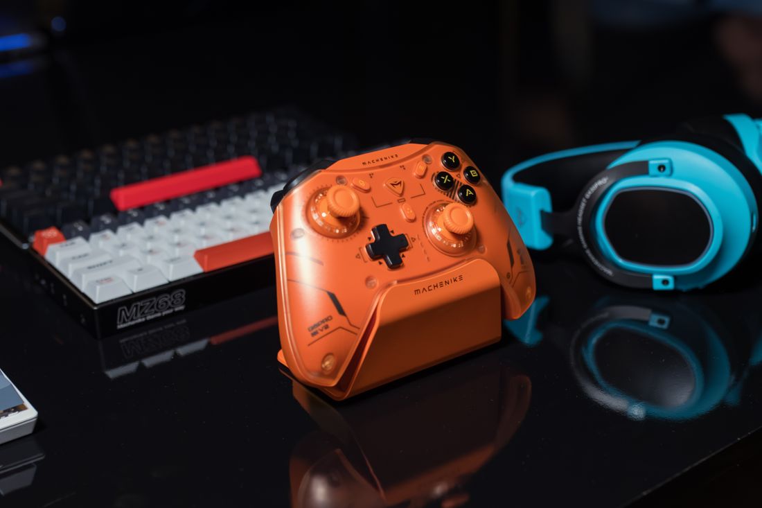 An orange game controller beside a keyboard and blue headset.